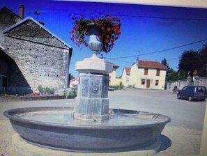 Una fuente de piedra con una maceta, rodeada por un muro de piedra y un edificio con techo rojo.
