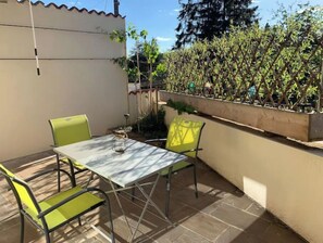 Un patio con mesa y sillas, rodeado por un muro bajo y un jardín.
