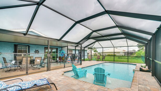 A covered outdoor pool area with lounge chairs and a glass-enclosed patio.