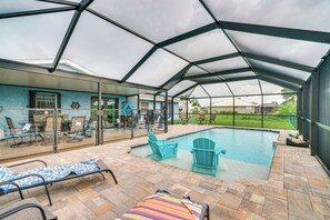 Et udendørs poolområde med parasol og liggestole, samt en patio med glasfacade.