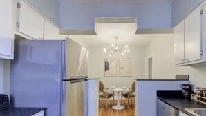 A modern kitchen with white cabinets, a stainless steel refrigerator, a dining area with a round table and chairs, and a chandelier. - Sweet Stay in Memphis (Memphis)