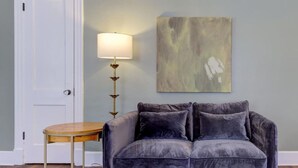 Et værelse med en grå sofa, et rundt træbord, en lampe og et billede på væggen.