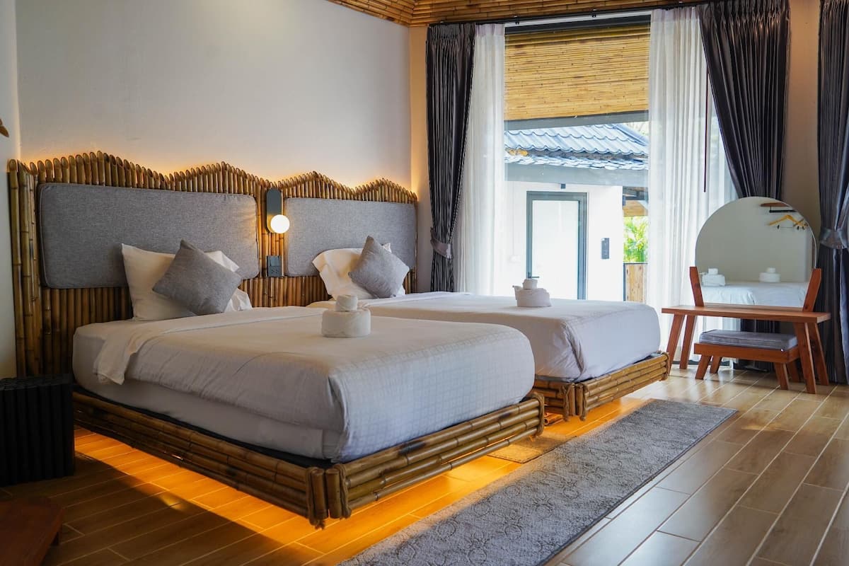 A double bed with a bamboo headboard, two bedside tables, a mirror, and a view of the outside.