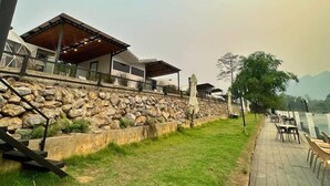 Un hotel a orillas del río con terraza exterior y un muro de contención de piedra.