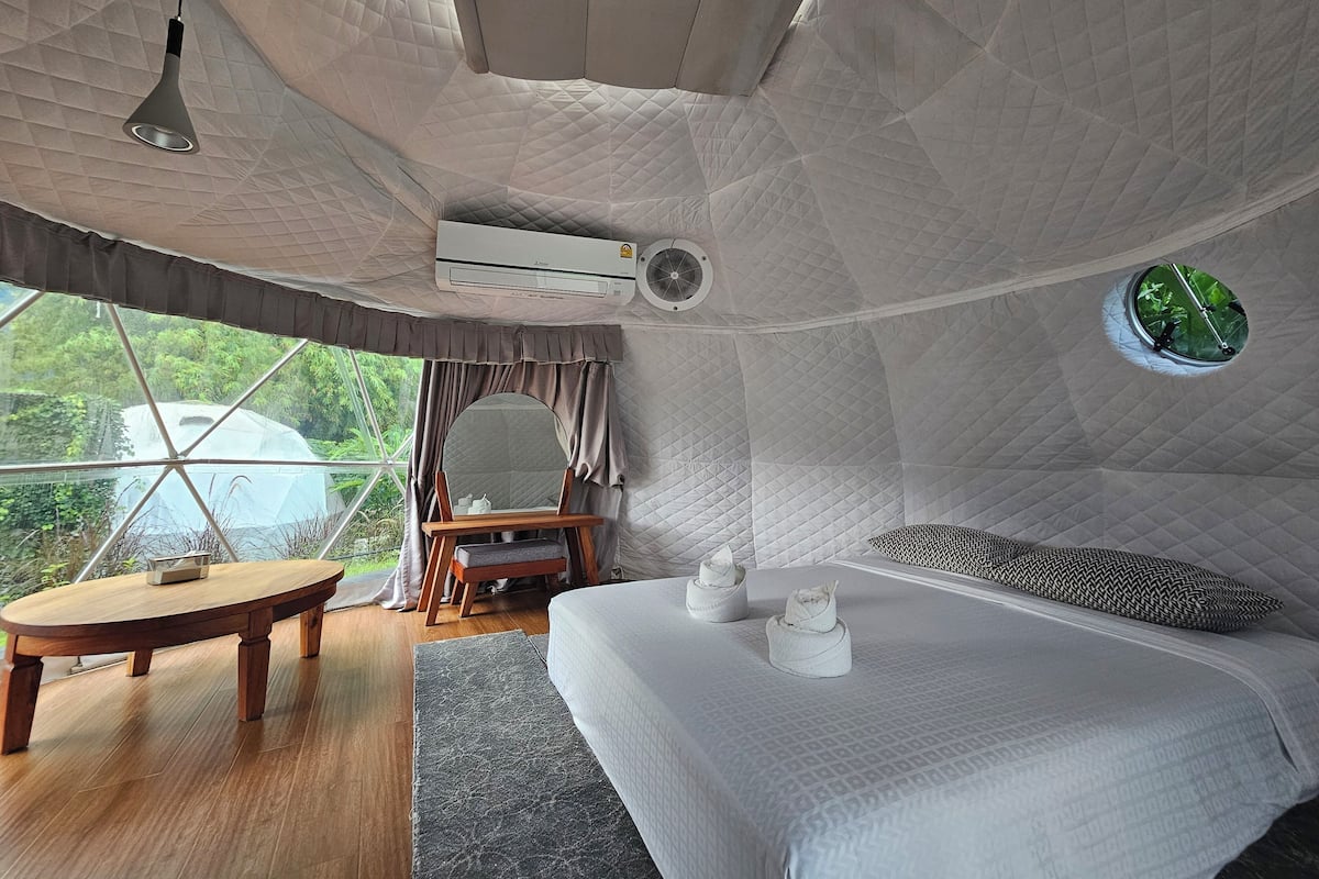 A cozy, uniquely shaped room with a bed, a small table, and a mirror.