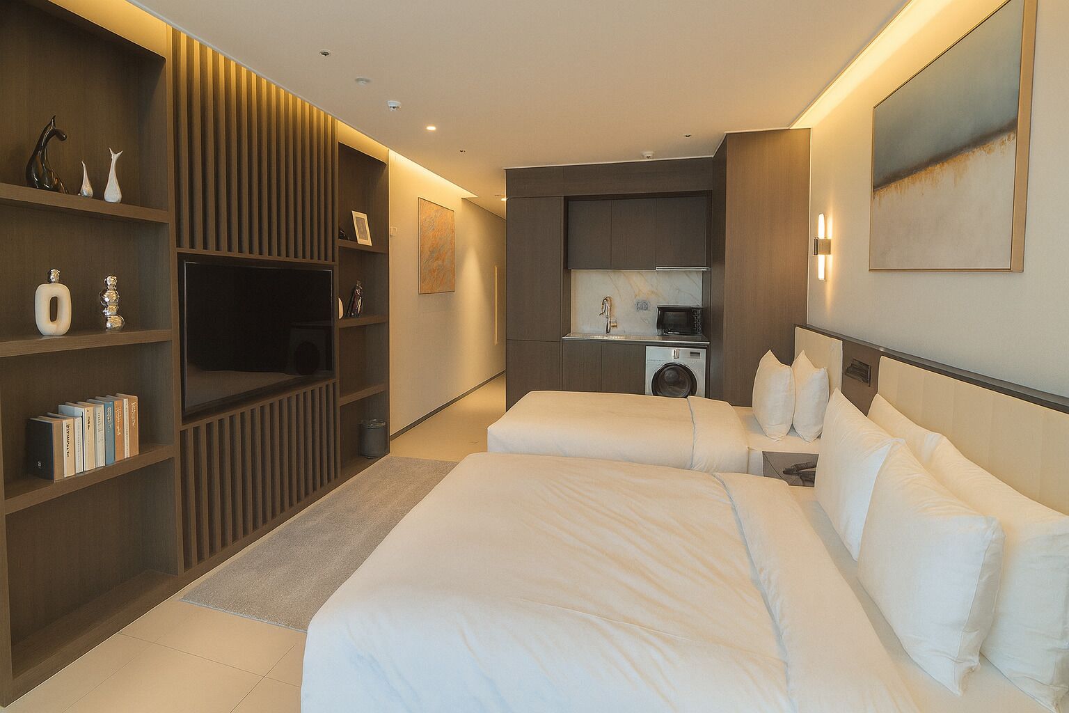 A modern hotel room with a large bed, built-in shelving, a small kitchenette, and a large mirror.