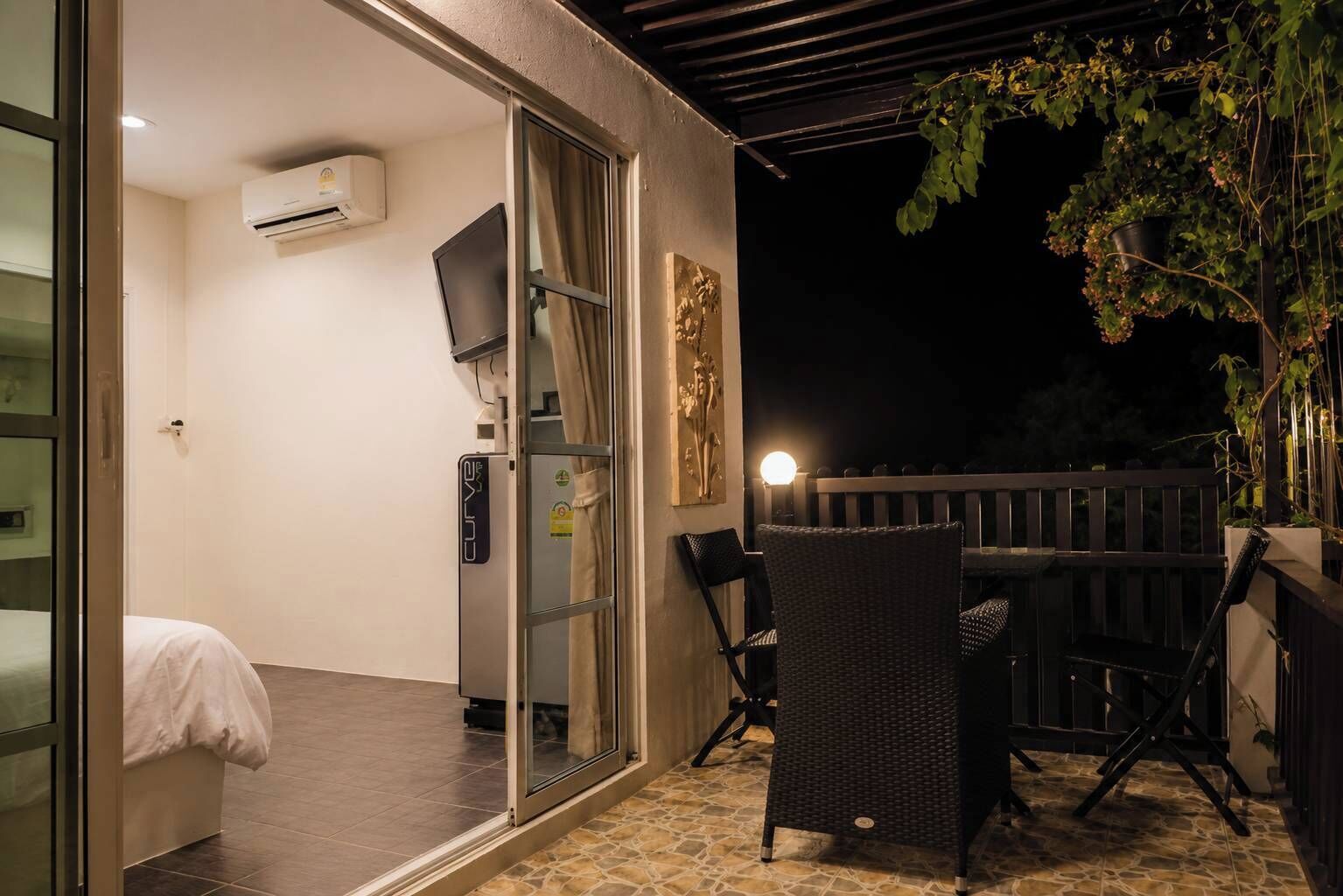 Ein Zimmer mit einem Bett, einem Fernseher, einem Fenster mit Vorhängen, einer Wand-Klimaanlage und einem kleinen Tisch mit Stühlen.