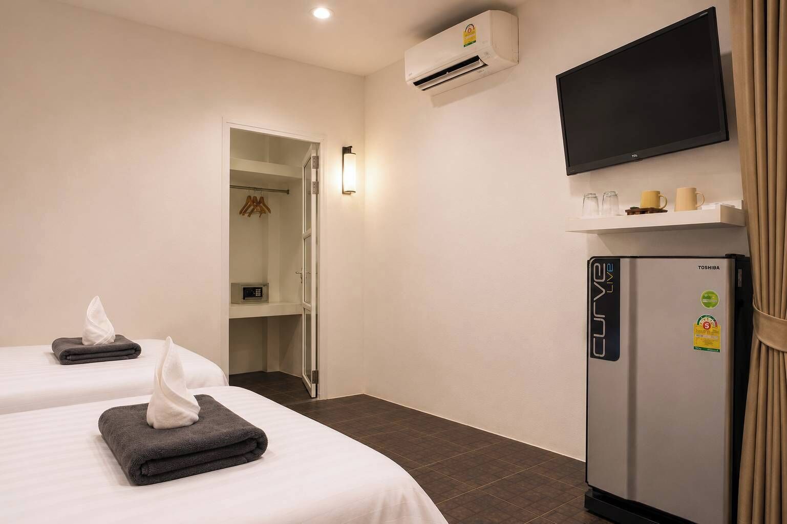 Habitación de hotel con dos camas, televisión, refrigerador y aire acondicionado.