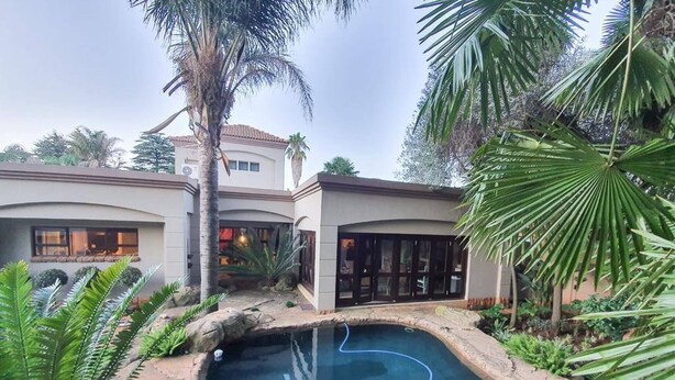 A pool surrounded by rocks and tropical plants, with a building in the background.