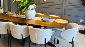 A dining area with a wooden table, six chairs, a potted plant, and decorative plates on the wall.