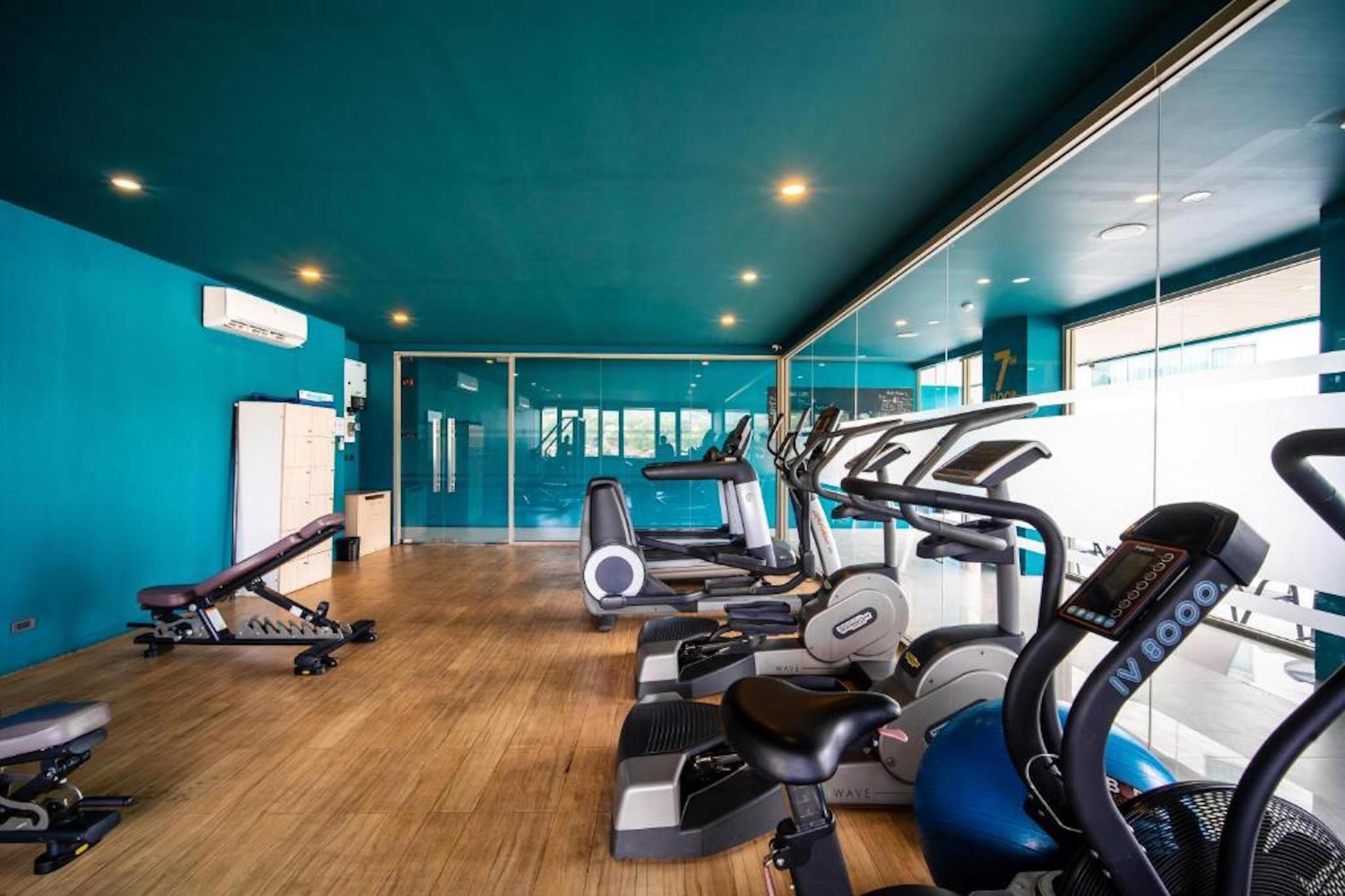 Un gimnasio con máquinas de cardio, bancos de pesas y un espejo grande.