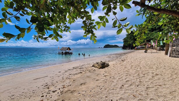 A beach with clear blue water, a wooden structure, and a sandy shore.