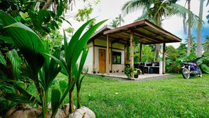 A small house with a porch, surrounded by lush greenery and palm trees.