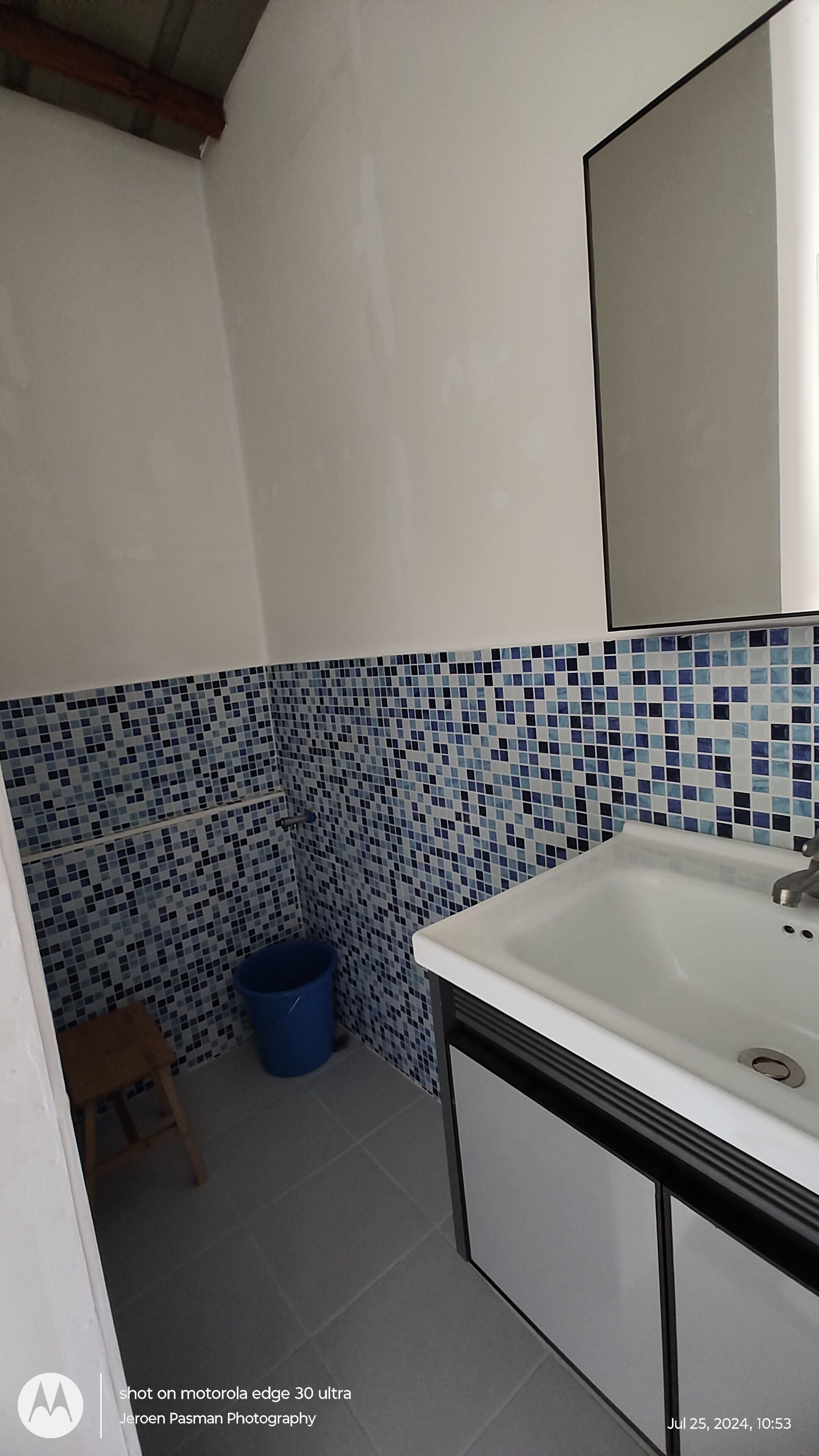 A bathroom with a white sink, blue mosaic tiles on the wall, and a blue trash bin.