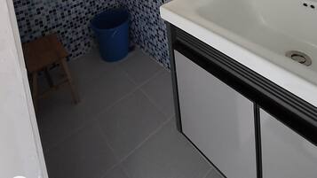 A bathroom with a white sink, blue mosaic tiles on the wall, and a blue trash bin.