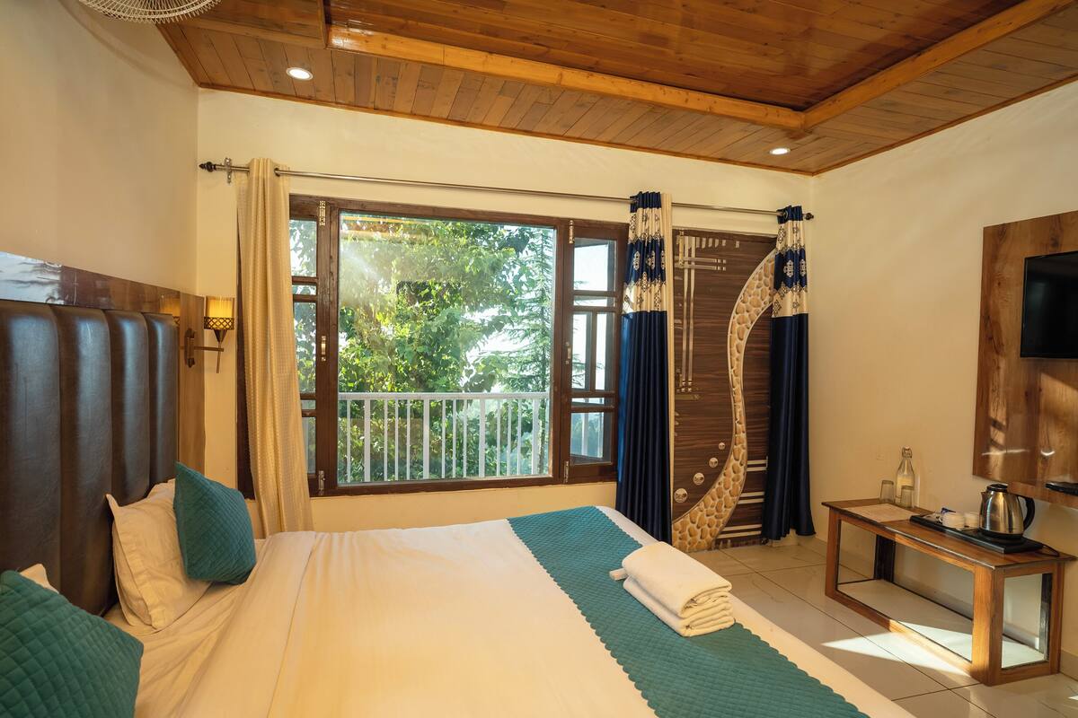 A hotel room with a large bed, a wooden headboard, a small table with a kettle, and a balcony view.