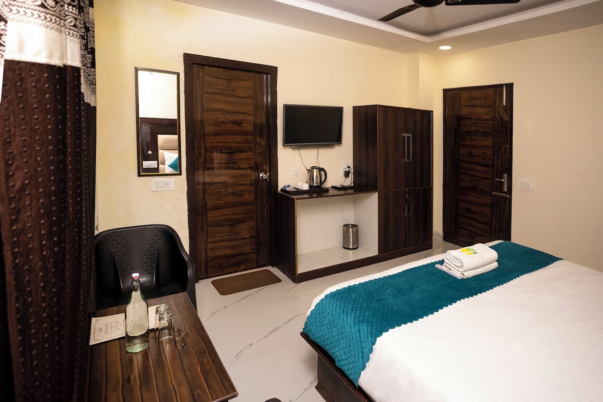 A hotel room with a bed, a desk with a chair, a television, and a wardrobe.