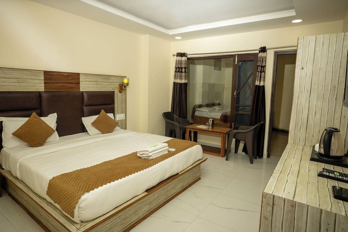 A hotel room with a large bed, a desk, a chair, and a wardrobe.