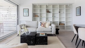 Ein modernes Wohnzimmer mit einem weißen Sofa, einem schwarzen Marmor-Couchtisch und einer großen weißen Bücherwand.