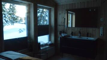 Enjoy a serene view of the snowy landscape from the large window in this cozy room, featuring a comfortable bed and a convenient bedside table with a lamp.