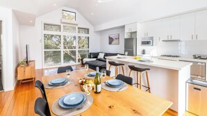 Una cocina moderna con armarios blancos, una isla central y un comedor con mesa de madera para cuatro.