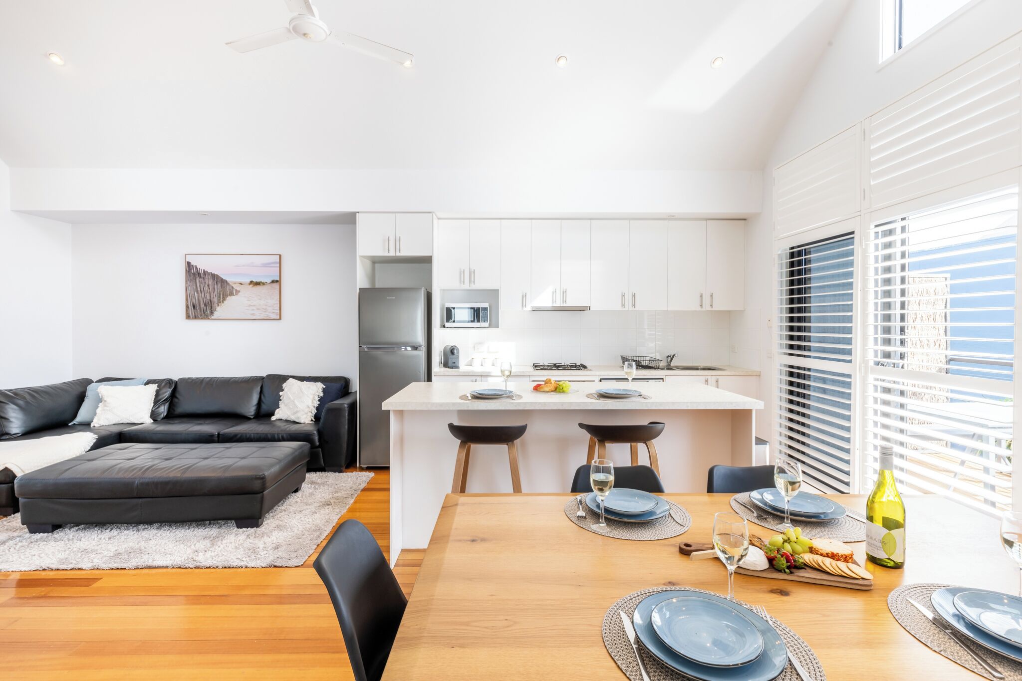 Una cocina moderna con armarios blancos, una isla central y un área de comedor con una mesa de madera dispuesta para dos personas.