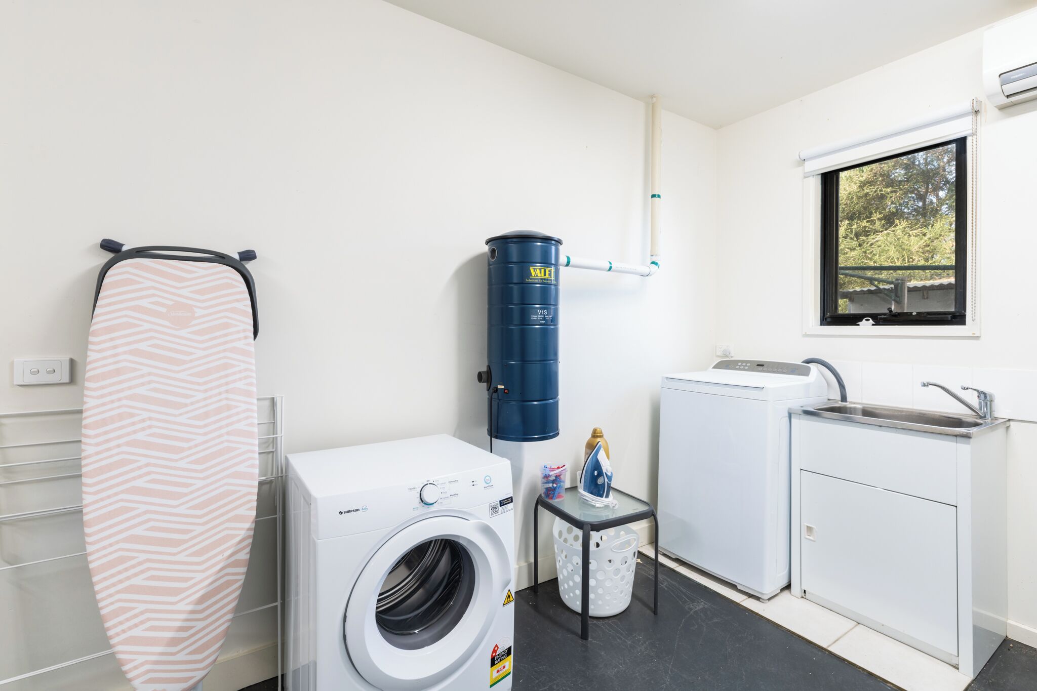 A compact laundry room with a washing machine, a dryer, a water heater, and a sink.