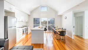 Una cocina moderna con armarios blancos, una isla central y un comedor con mesa y sillas de madera.