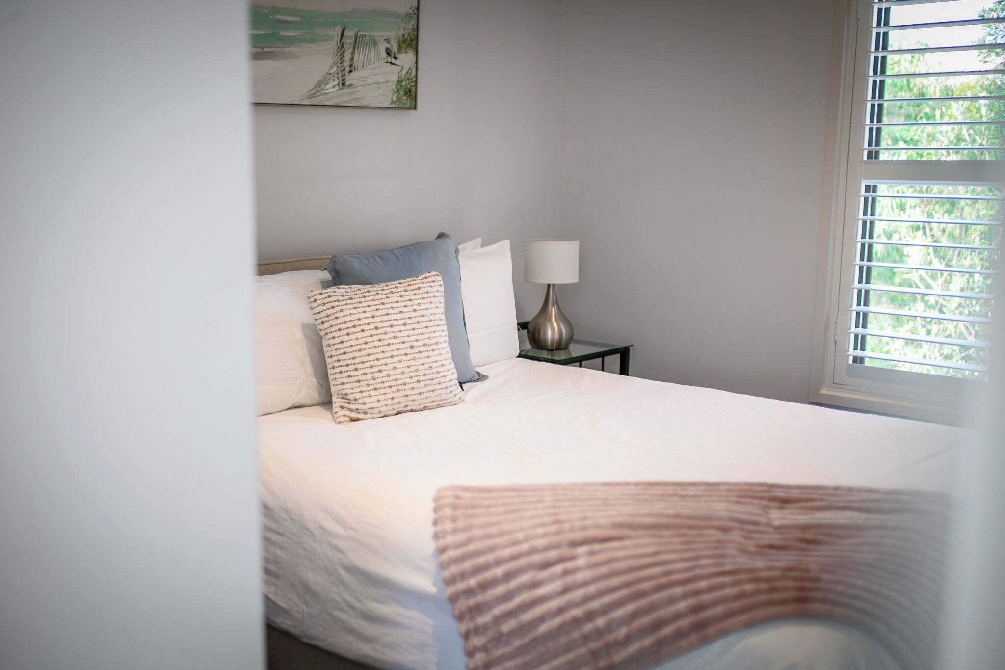 A neatly made bed with a white comforter and a striped throw blanket.