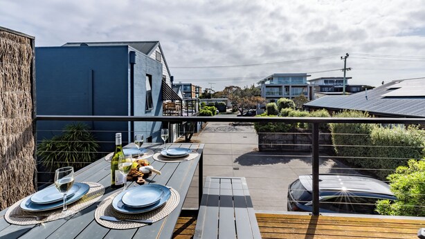 Un área de comedor al aire libre con terraza de madera, una mesa para dos personas dispuesta con platos, vasos y una botella de vino.