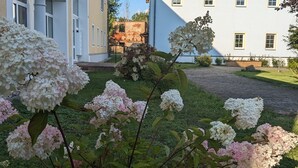 A building with a red-tiled roof, white walls, and a garden with hydrangea flowers. - Apartment 'Ferienwohnung Wiesenduft' with Shared Pool, Shared Terrace and Wi-Fi (Klipphausen)