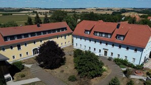 A large building with a red roof, multiple windows, and a central courtyard with trees. - Apartment 'Ferienwohnung Wiesenduft' with Shared Pool, Shared Terrace and Wi-Fi (Klipphausen)