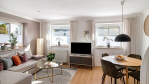 A modern living room with a sofa, coffee table, TV, dining table, chairs, and a hanging light fixture. - Apartment 'Fewo Christi' with Wi-Fi (Weißensberg)