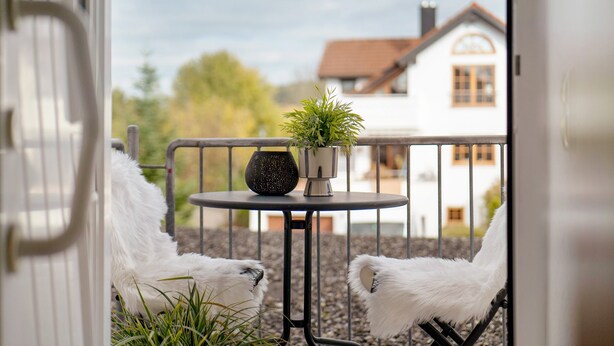 A balcony with two white chairs, a small table with a potted plant, and a white building in the background. - Apartment 'Fewo Christi' with Wi-Fi (Weißensberg)