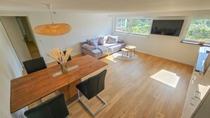 Un espace de vie moderne comprenant une table à manger en bois, des chaises noires, un canapé et une petite table ronde.