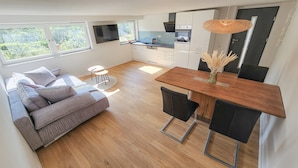 Une cuisine moderne dotée d’un four encastré, un coin repas avec une table et des chaises en bois, un canapé gris et une petite table ronde avec une chaise.