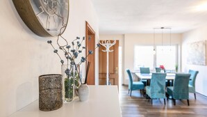 Ein Essbereich mit Tisch und Stühlen, einem dekorativen Wandbild und einer Vase mit blauen Blumen.