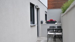 Pieni patio, jossa on pöytä ja tuoleja, kukilla koristeltu ruukku ja ikkuna.