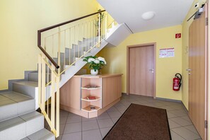 A staircase with a wooden handrail, a reception desk with a vase of flowers, a fire extinguisher, and a closed door.