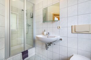 A modern bathroom with a glass shower enclosure, a white sink with a glass shelf above it, and a mirror.