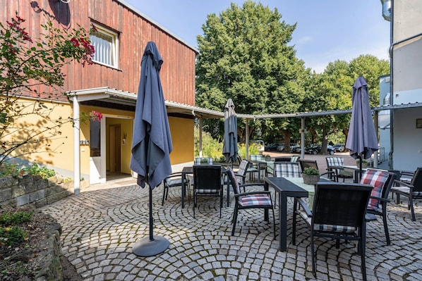 A courtyard with outdoor seating, a building with a red facade, and a tree in the background.