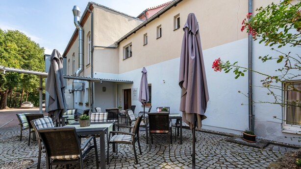 An outdoor patio with tables and chairs, umbrellas, and a building with a tiled roof.
