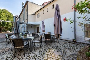 Une terrasse extérieure avec des tables et des chaises, des parasols et un bâtiment doté d’un toit en tuiles.