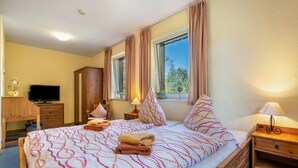 Ein Hotelzimmer mit Bett, Fernseher, Schreibtisch, Kleiderschrank und einem Fenster mit Vorhängen.