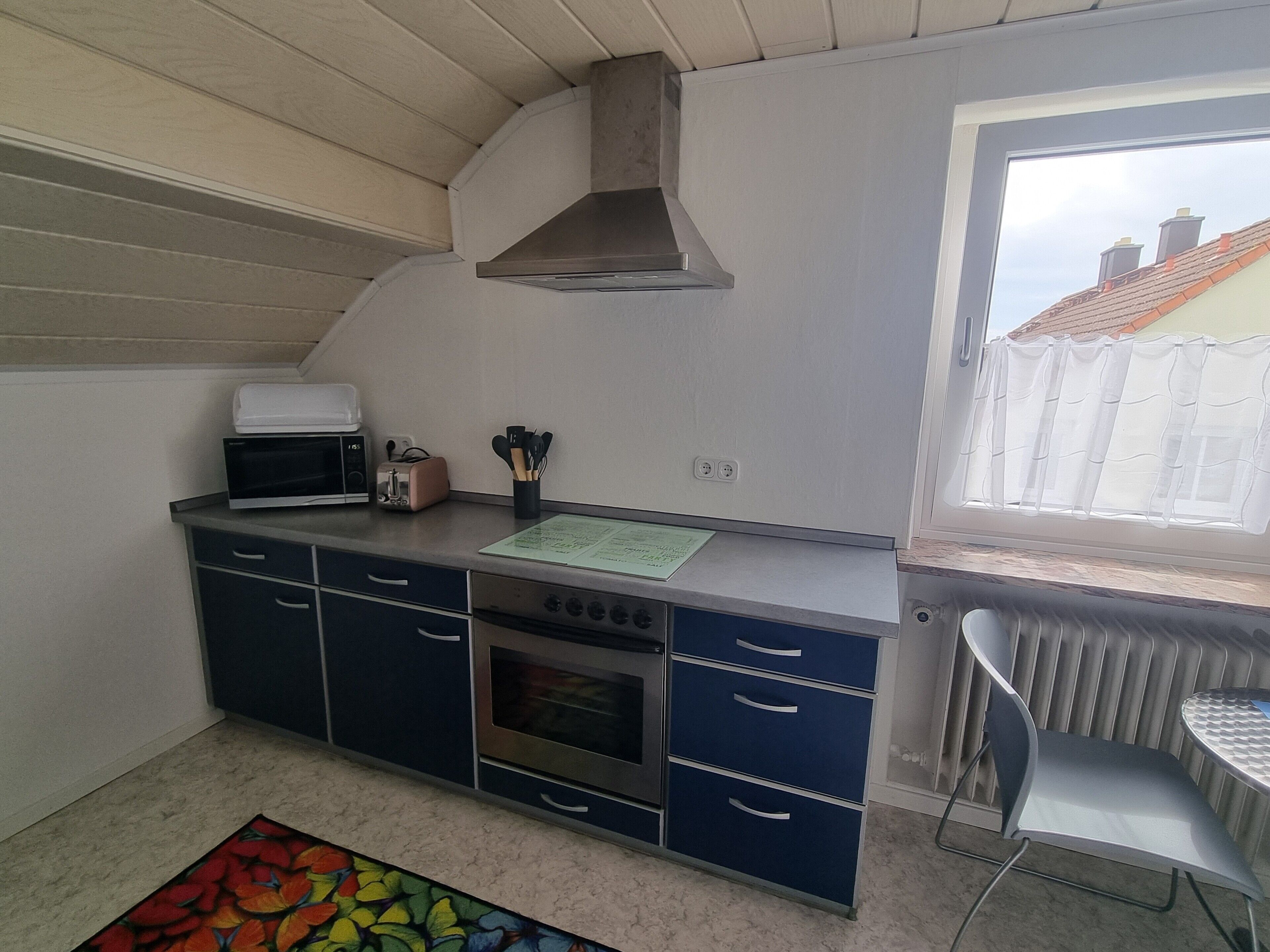 Une cuisine compacte équipée d’un four à micro-ondes, d’un grille-pain et d’une cuisinière, une fenêtre donnant sur des immeubles et un radiateur.