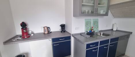 A compact kitchen with a sink, a coffee maker, a kettle, and a trash bin.