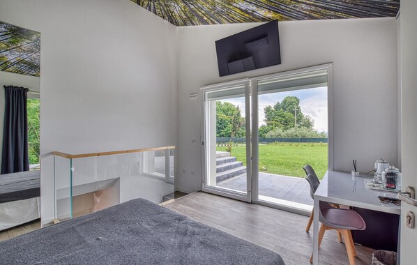 Une chambre moderne dotée d’une porte-fenêtre coulissante donnant sur un jardin, d’un bureau avec une chaise et d’un escalier.