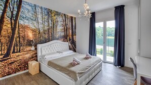 Een slaapkamer met een grote bosmuur, een wit bed en uitzicht door de glazen deur.