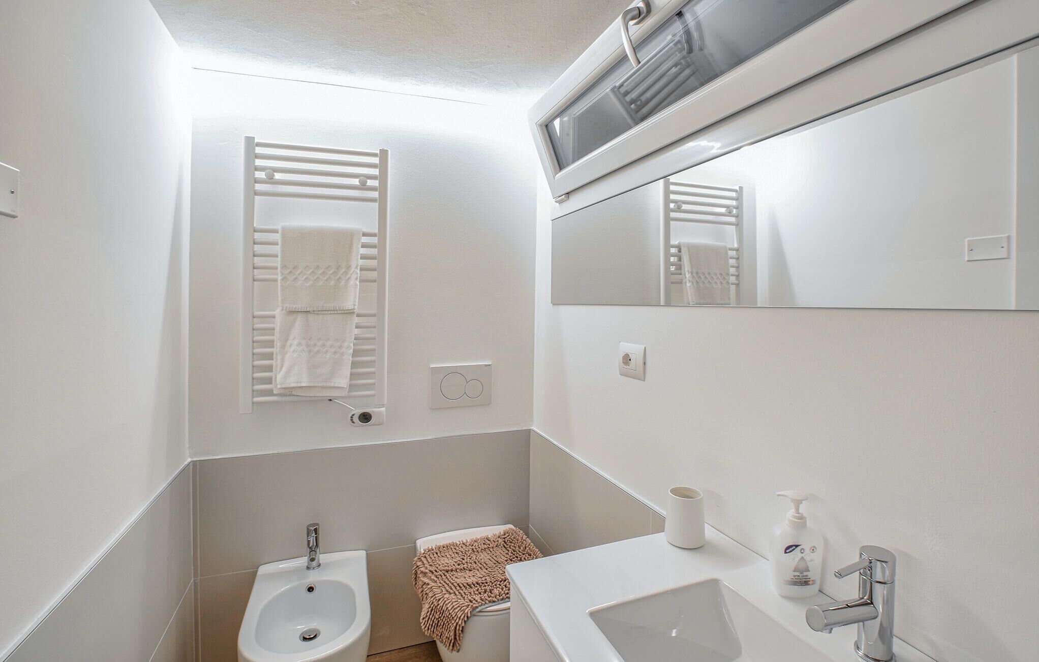 A bathroom with a bidet, a sink, a mirror, and a towel rack.