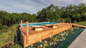 Een houten terras met een zwembad, omringd door groen.